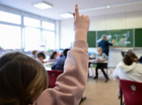 Ein Kind streckt die Hand in einer Schulklasse in die Höhe.