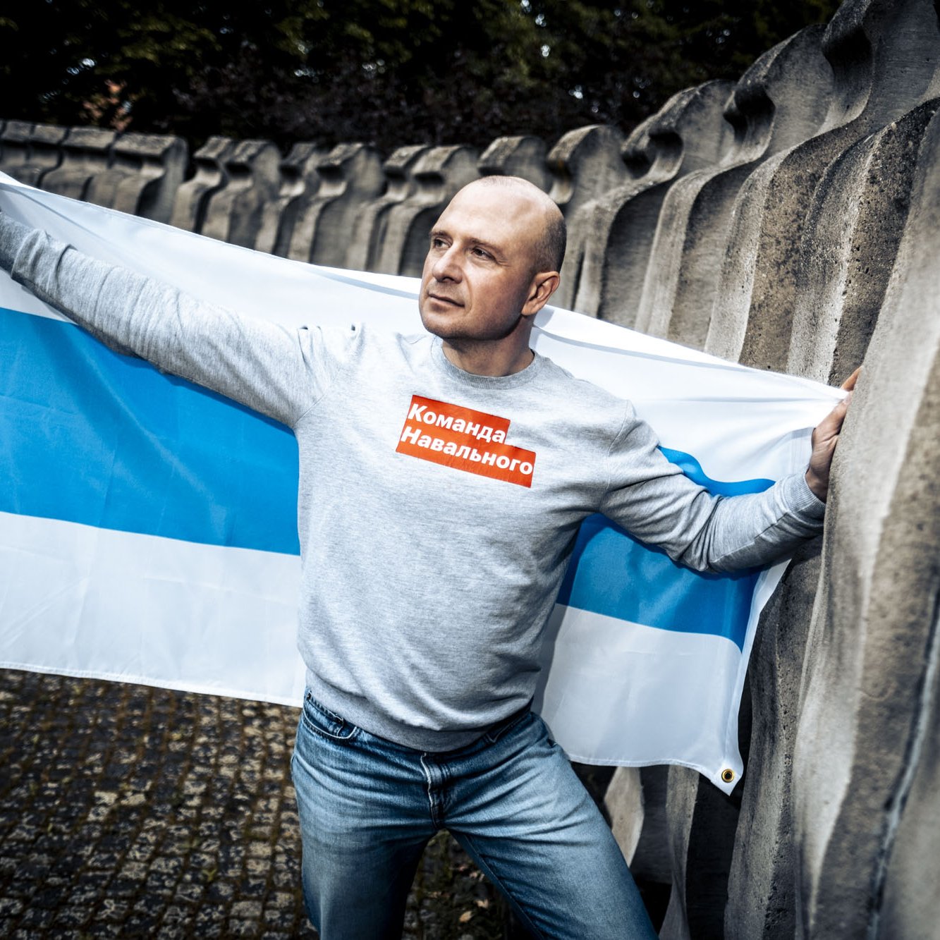 Mann auf einem öffentlichen Platz in Freiburg. Im Hintergrund ist die weiß-blau-weiße-Flagge, ein Symbol der Proteste gegen den russischen Überfall auf die Ukraine, zu sehen.