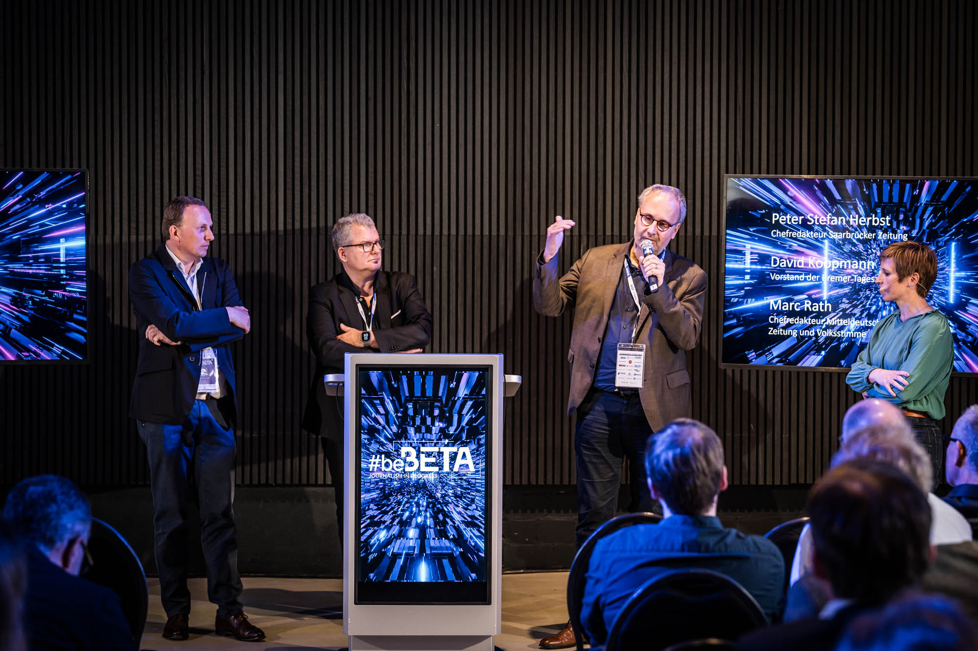 Vier Männer und eine Frau stehen auf einer Bühne in einer Diskussion